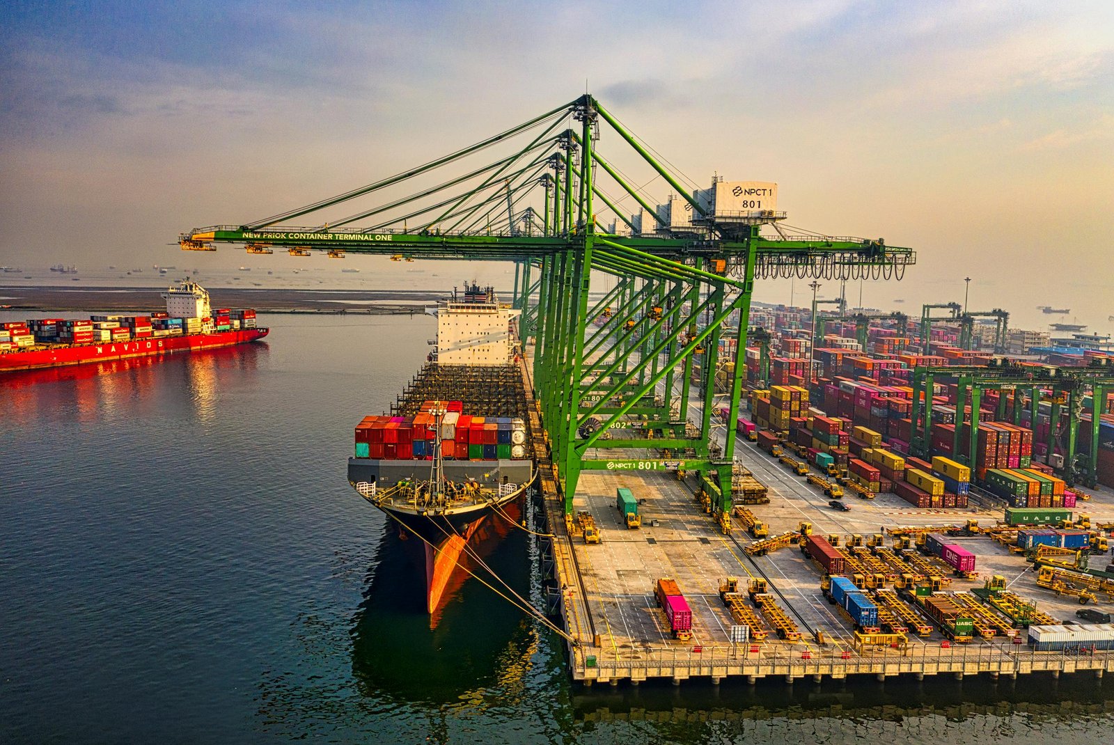 A bustling aerial view of a container port in North Jakarta, Indonesia with ships and cranes.